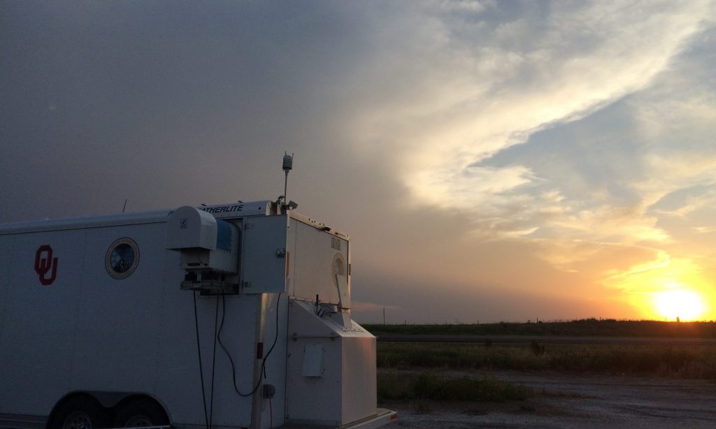 Instrument trailer in front of a sunset in a sky half-covered by an anvil cloud and over an empty field. 