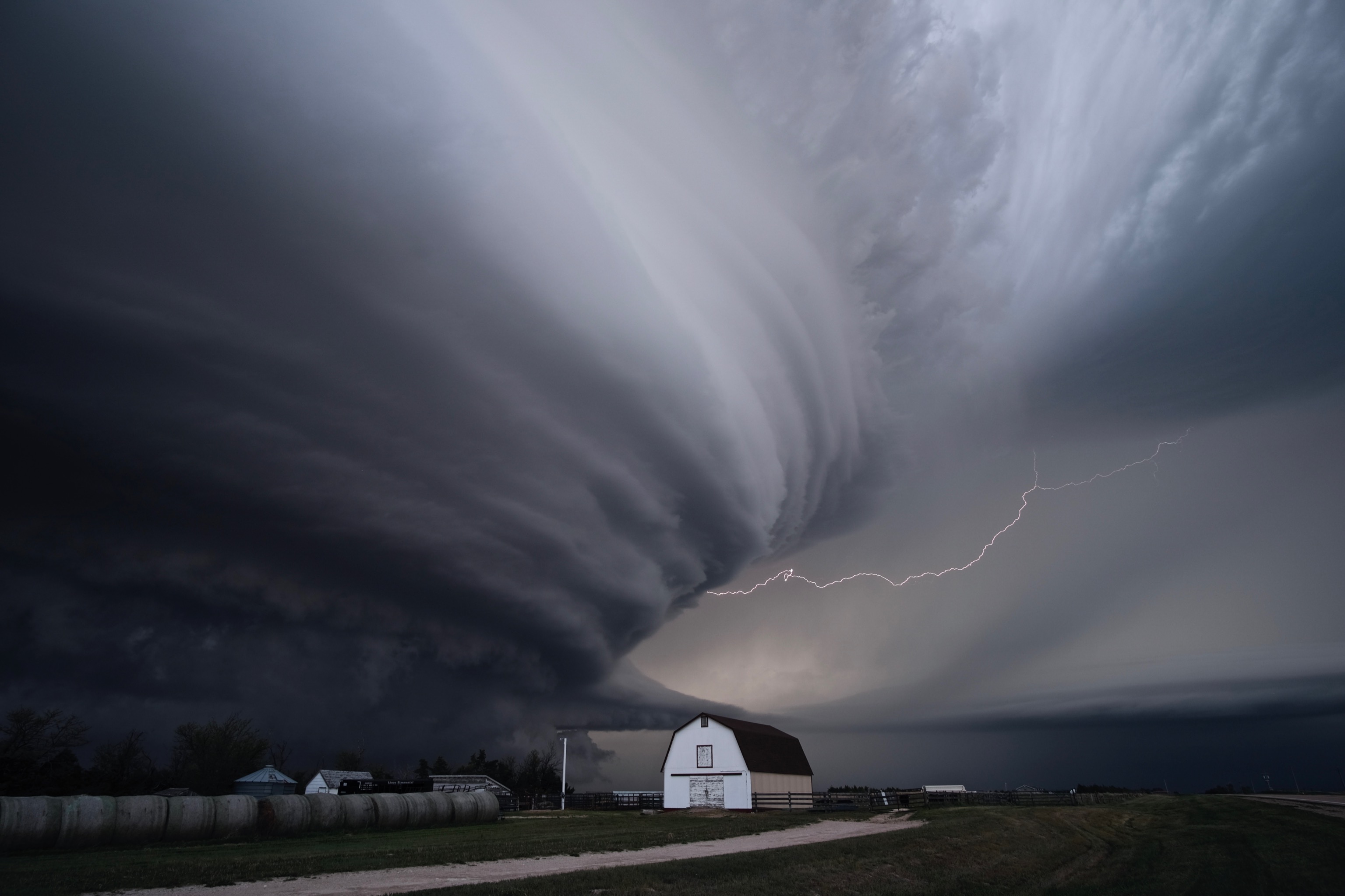 A supercell thunderstorm with lightning and a barn.