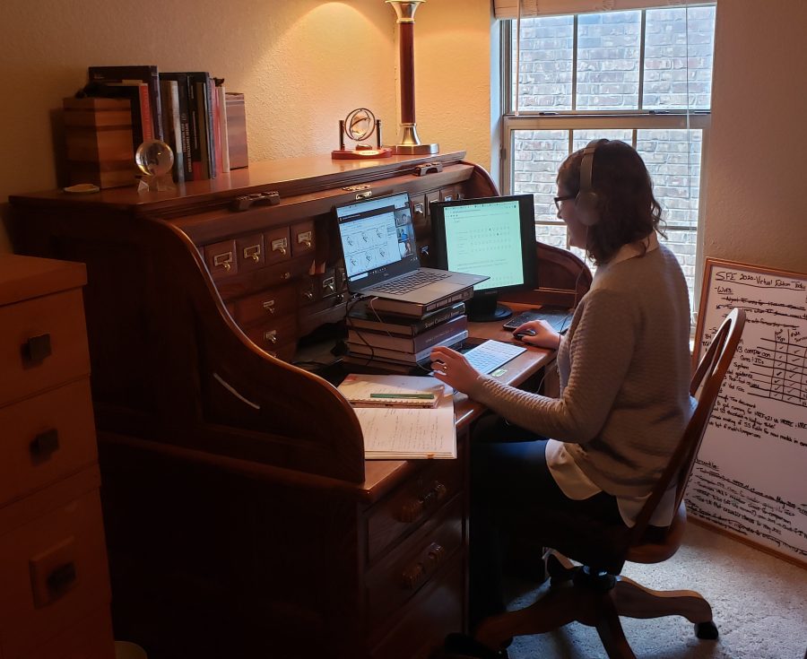A woman sitting in a chair in her home office looking at two computer screens in front of her.