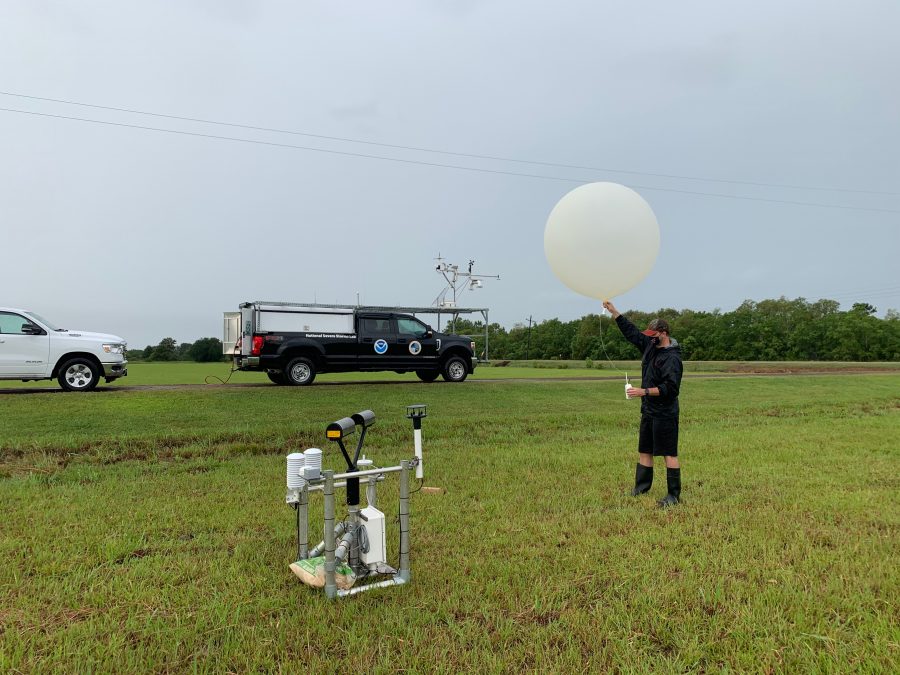A researcher standing in a field holding a weather balloon above his head, waiting to release it.