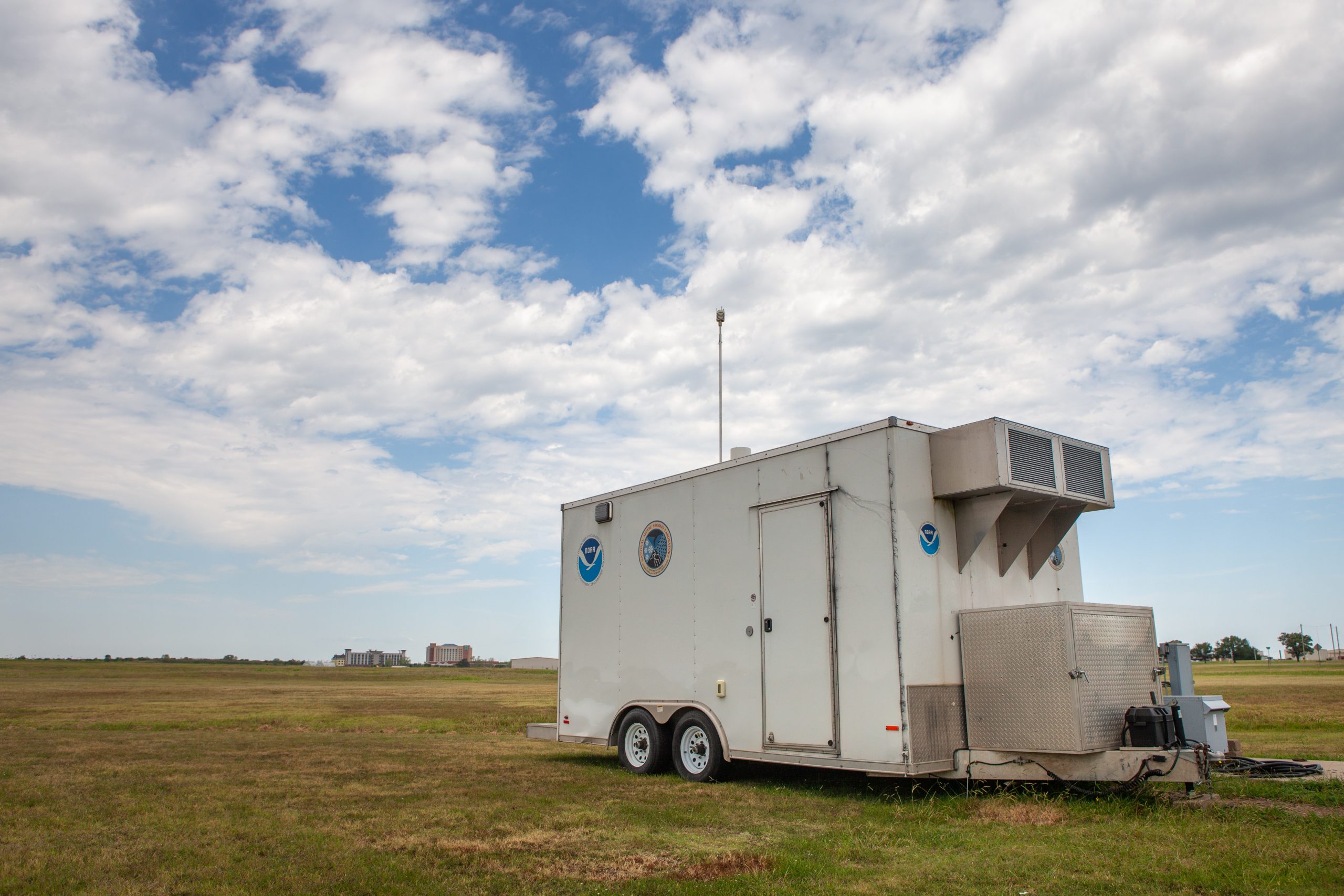 A mobile research trailer parked in a grassy field. The sky is cloudy and blue above.