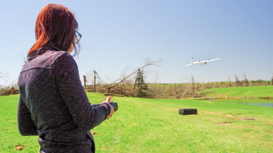 A woman hold a remote control, which flies a UAS in the distance.