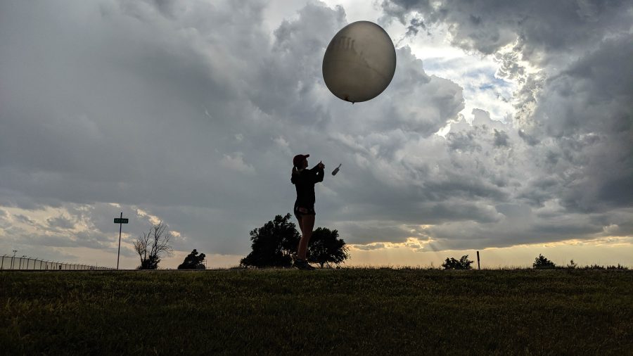 Woman launching weather balloon at sunset under cloudy sky